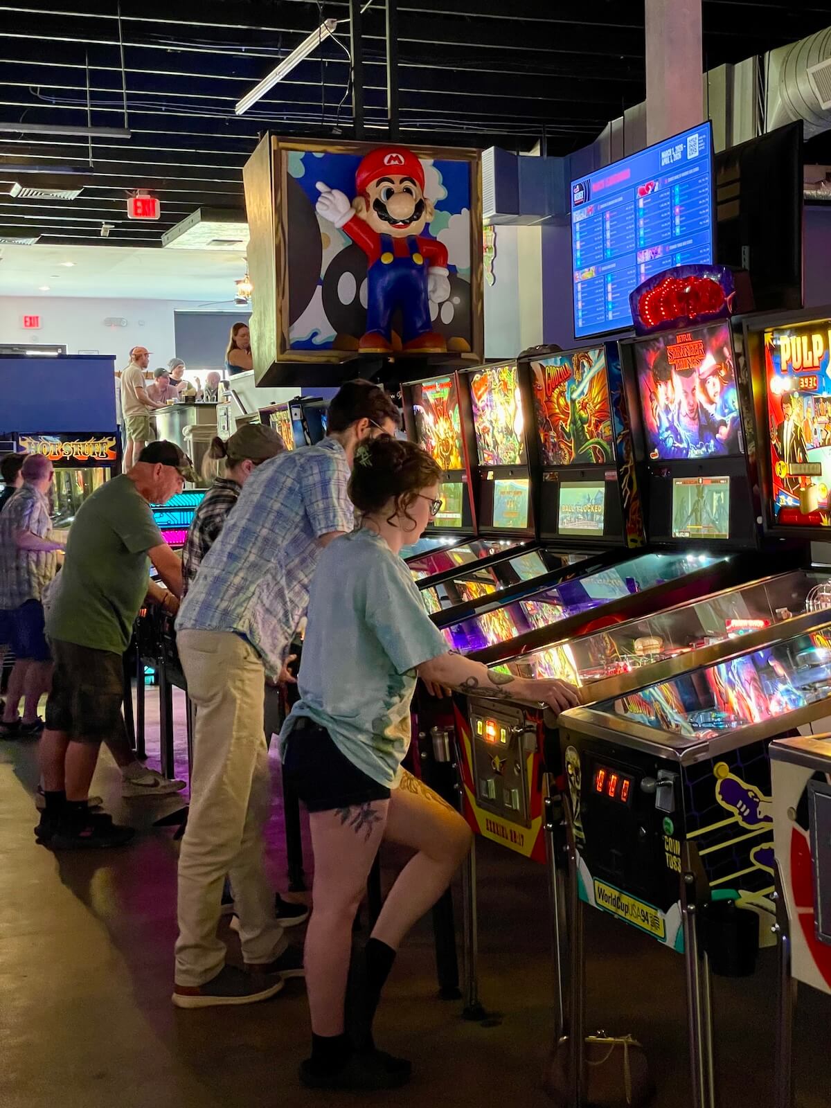 Pleople playing at a row of pinball games at Super Abari Game Bar in Optimist Park Charlotte