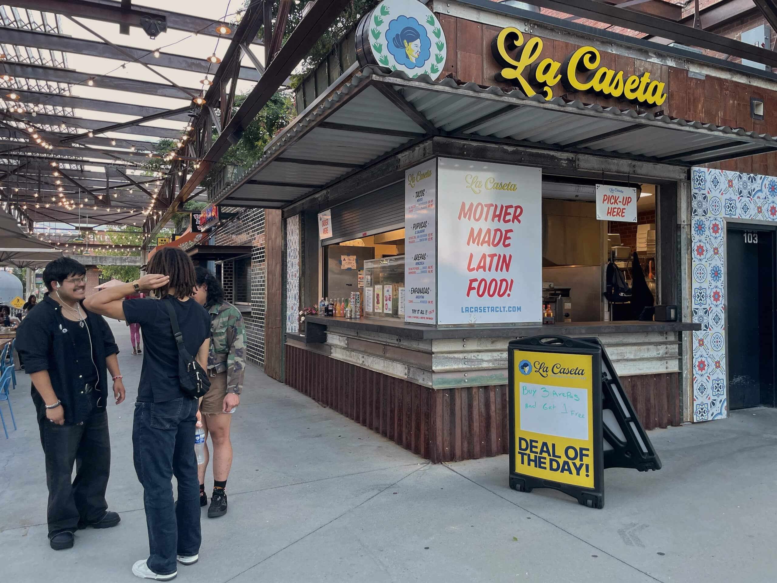 Three people standing outside an outdoor food stall at Camp North End in Charlotte
