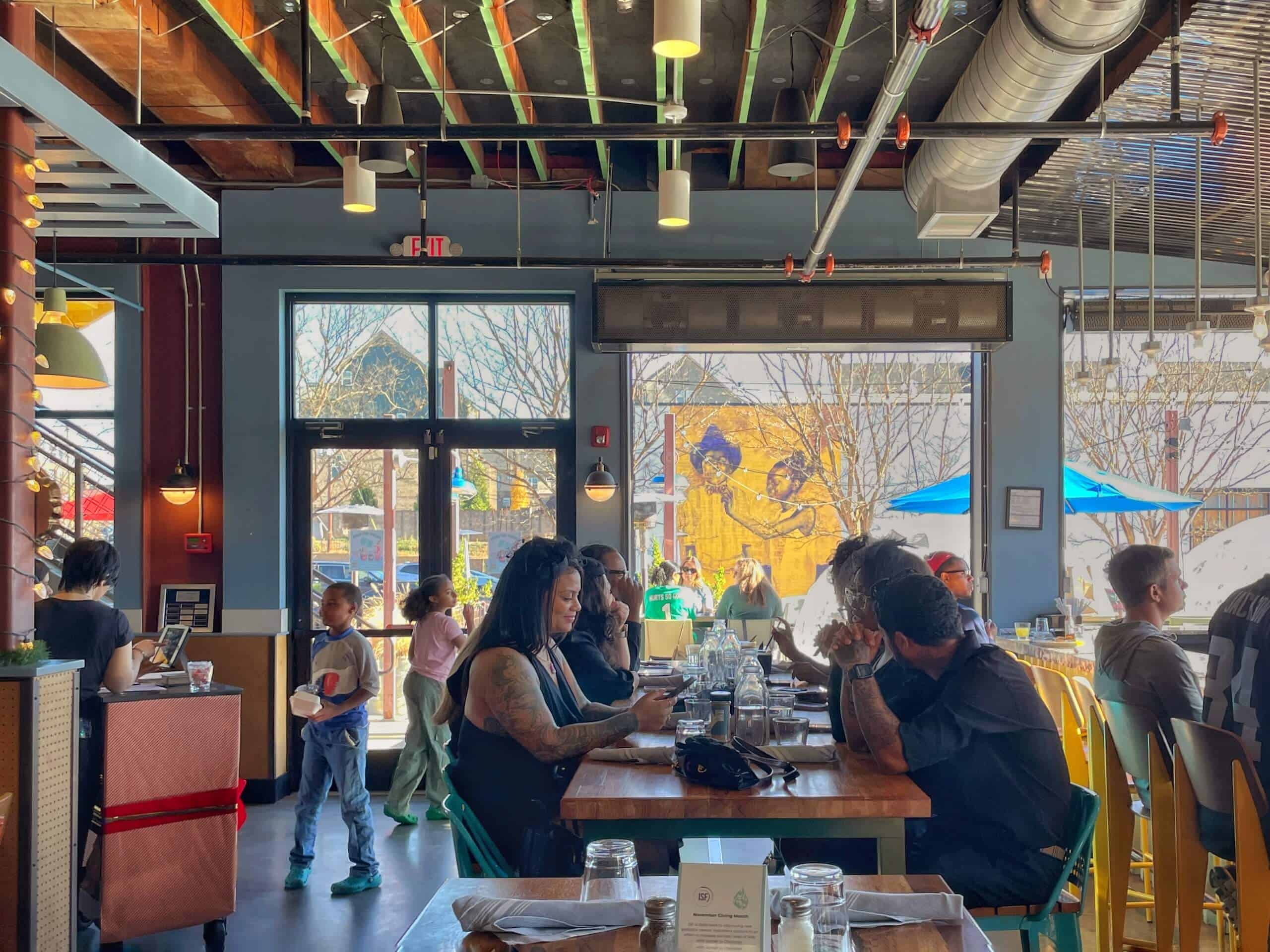 People eating brunch at State of Confusion in LoSo Charlotte. The view is from the inside of the restaurant looking out toward the patio, with a mural visible from across the street.