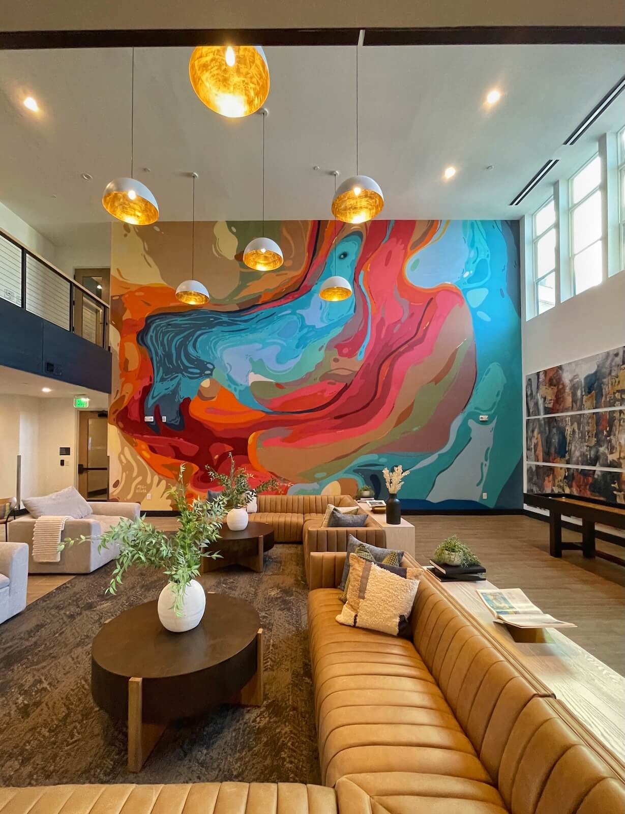 Lobby at Solis LoSo apartments in Charlotte. High ceilings with brightly colored, full wall mural along with leather sectional sofa and contemporary lighting. 