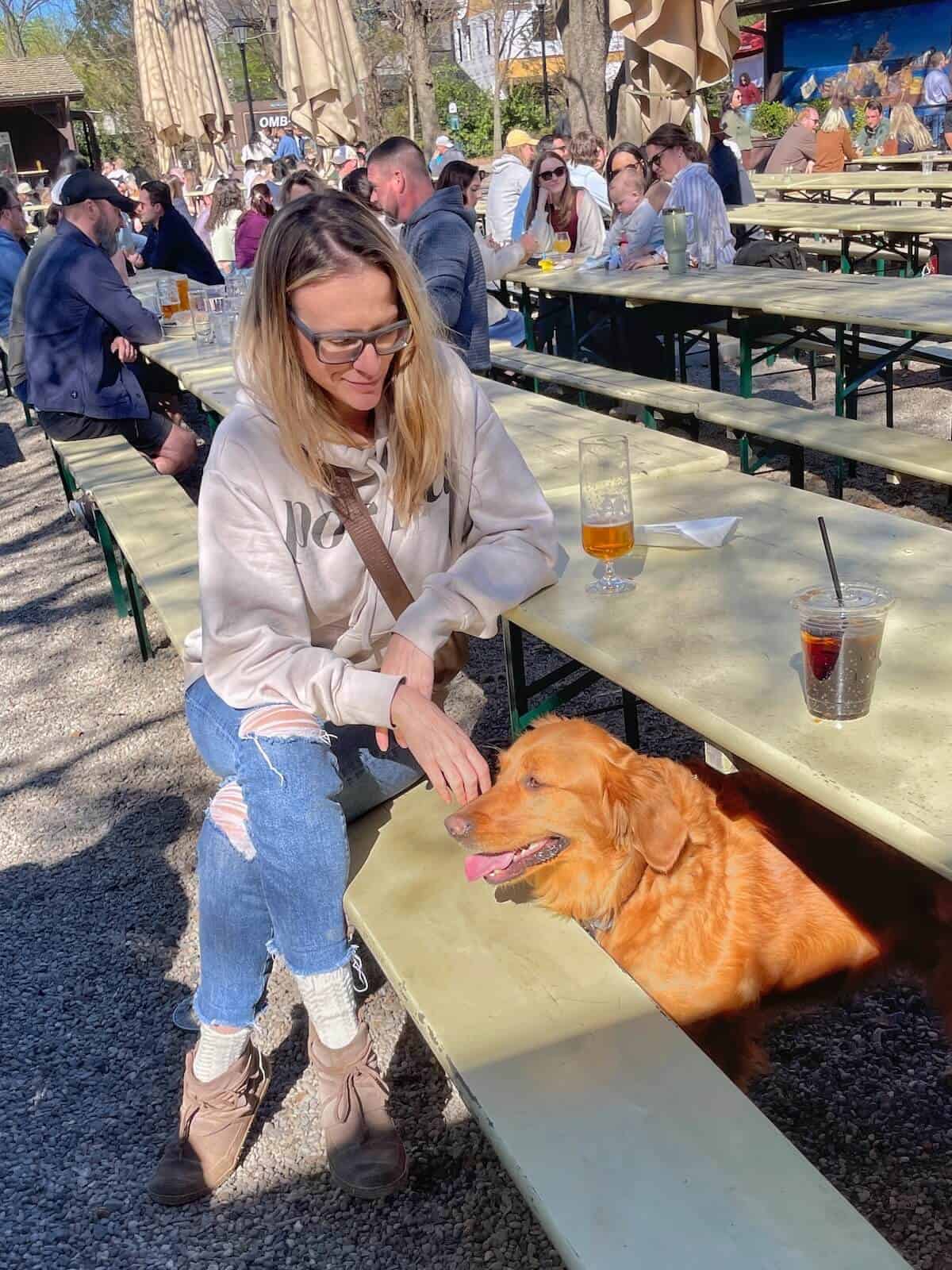 Woman sitting at a picnic table with a golden retriever poking its head out from under the table