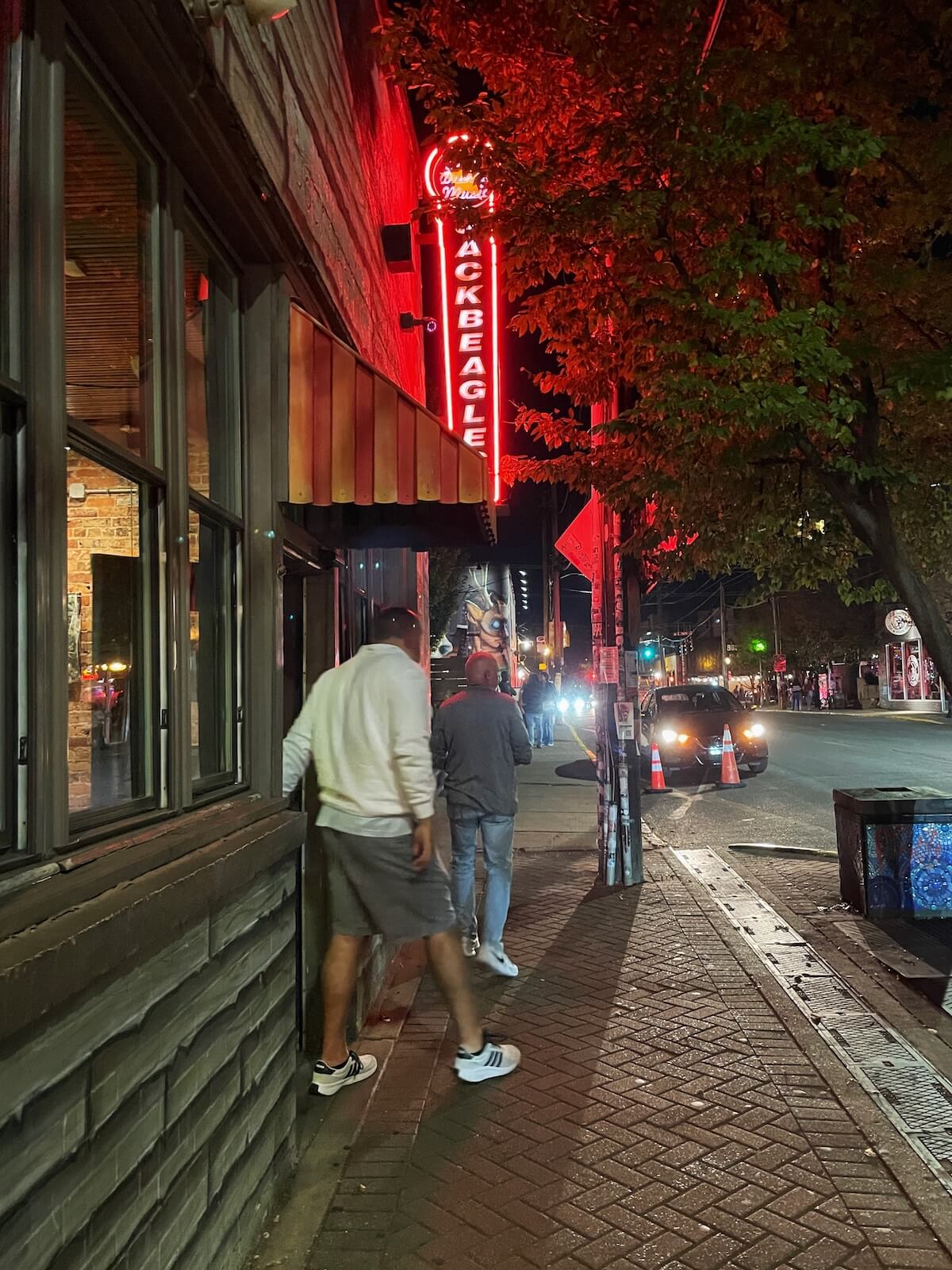 Glowing red sign says Jack Beagles. Two people exiting a neighborhood bar in NoDa Charlotte