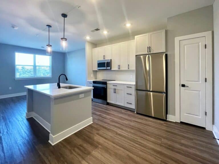 Modern kitchen with white cabinets, stainless steel refrigerator, and island in an apartment at Matheson Mill NoDa in Charlotte.