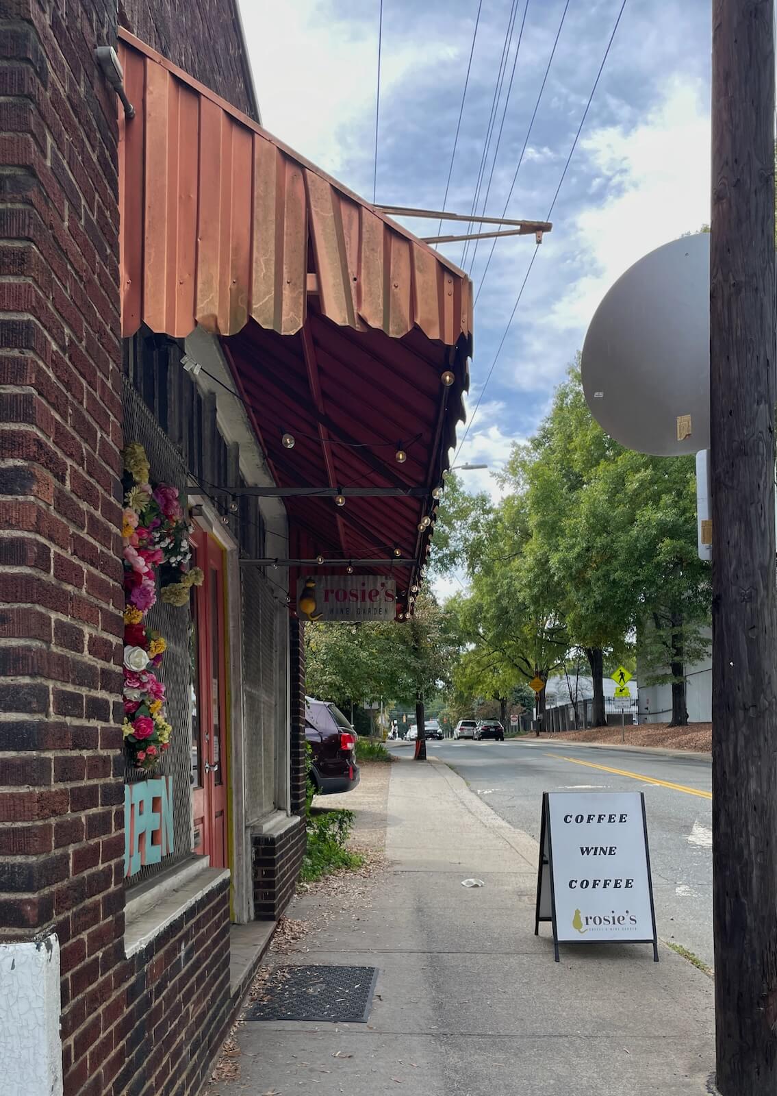Striped awning marks the entrance to Rose's Cafe and Wine Garden, with a sandwich board sign noting coffee