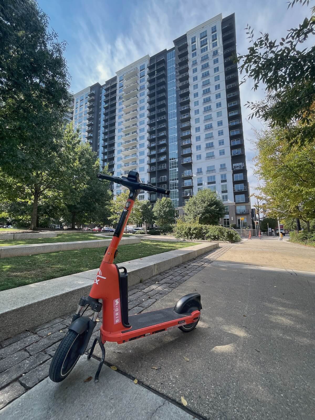 Orange scooter parked on a sidewalk in front of high rise apartment building in Uptown Charlotte