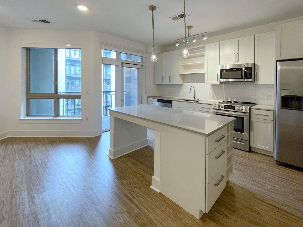 Kitchen with contemporary white cabinets, and a waterfall island with seating on both sides in an apartment at Savoy in Uptown Charlotte.