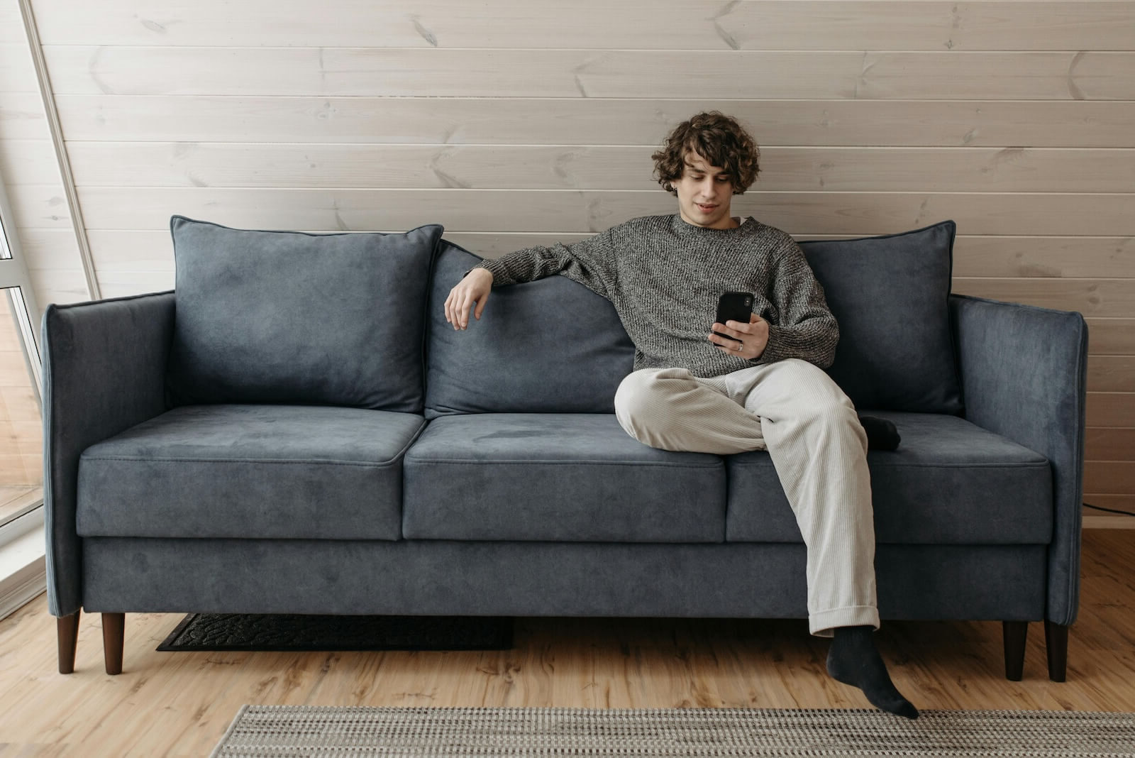 Man sitting on a blue sofa in a comfortable position while holding a cell phone.