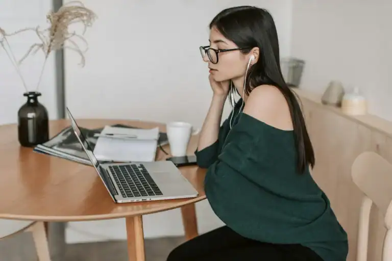 Woman sitting at a table with a laptop and notepads.