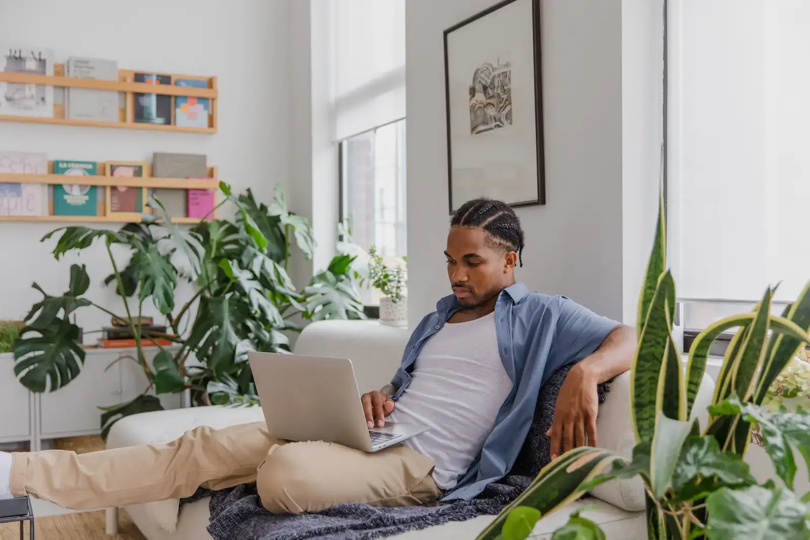 Man sitting on a sofa in a living room flooded with natural light and several plants.